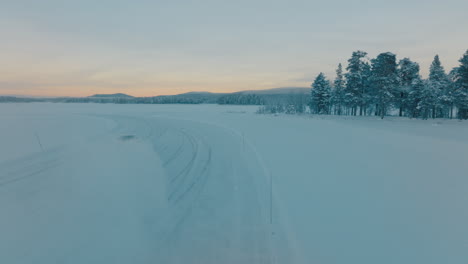 Vista-Aérea-Siguiendo-Al-Conductor-Norbotten-A-La-Deriva-En-El-Lago-Congelado-De-Hielo-De-Laponia-En-La-Nieve-Del-Amanecer