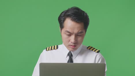 아시아 남성 조종사가 노트북을 바라보며 소리를 지르며 녹색 스크린 배경 스튜디오에 서서 골을 축하하고 있습니다.
