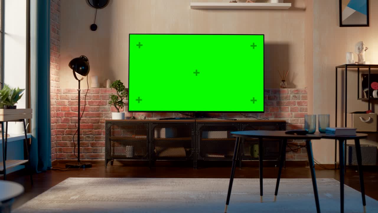 Stylish Loft Apartment Interior with TV Set with Green Screen Mock Up Display Standing on Television Stand. Empty Living Room at Home with Chroma Key Placeholder on Monitor. Zoom In Shot.