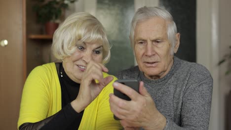 Pretty-mature-senior-couple-grandparents-enjoy-online-shopping-on-phone-at-home