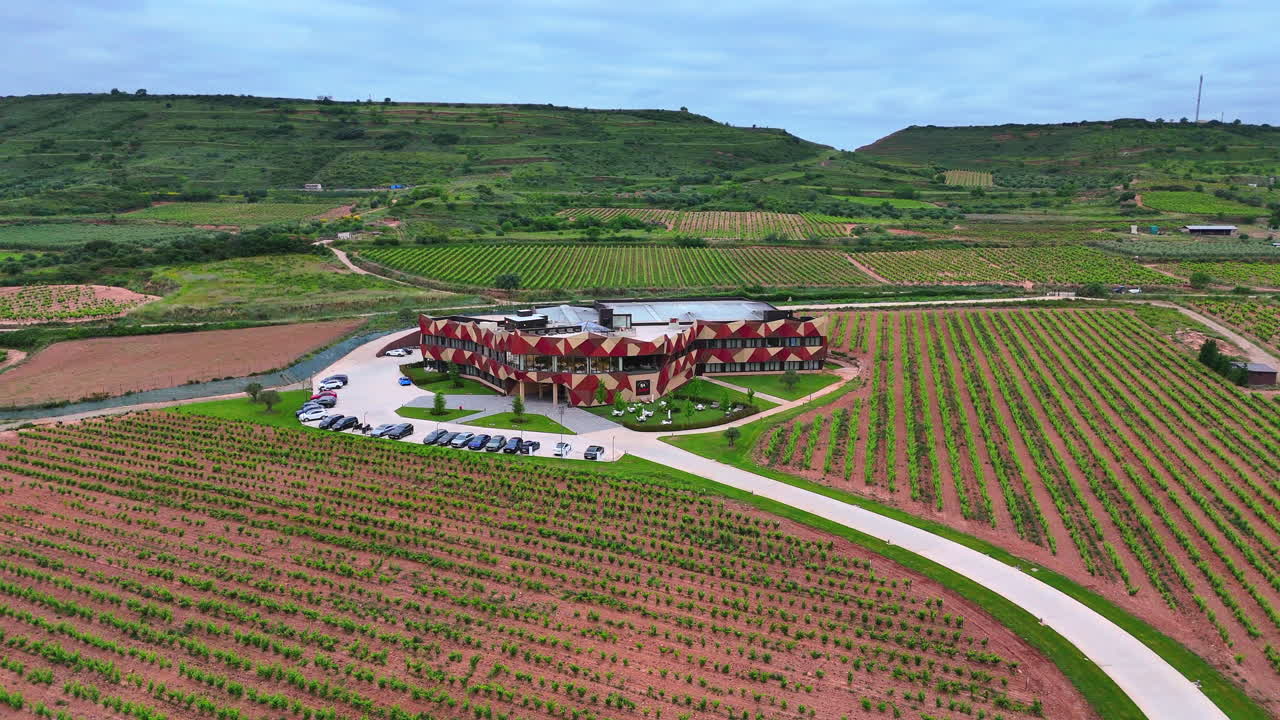 Orbiting aerial view of a modern winery surrounded by green vineyards in La Rioja, Spain. Scenic agricultural landscape, perfect viticulture setting in renowned wine region