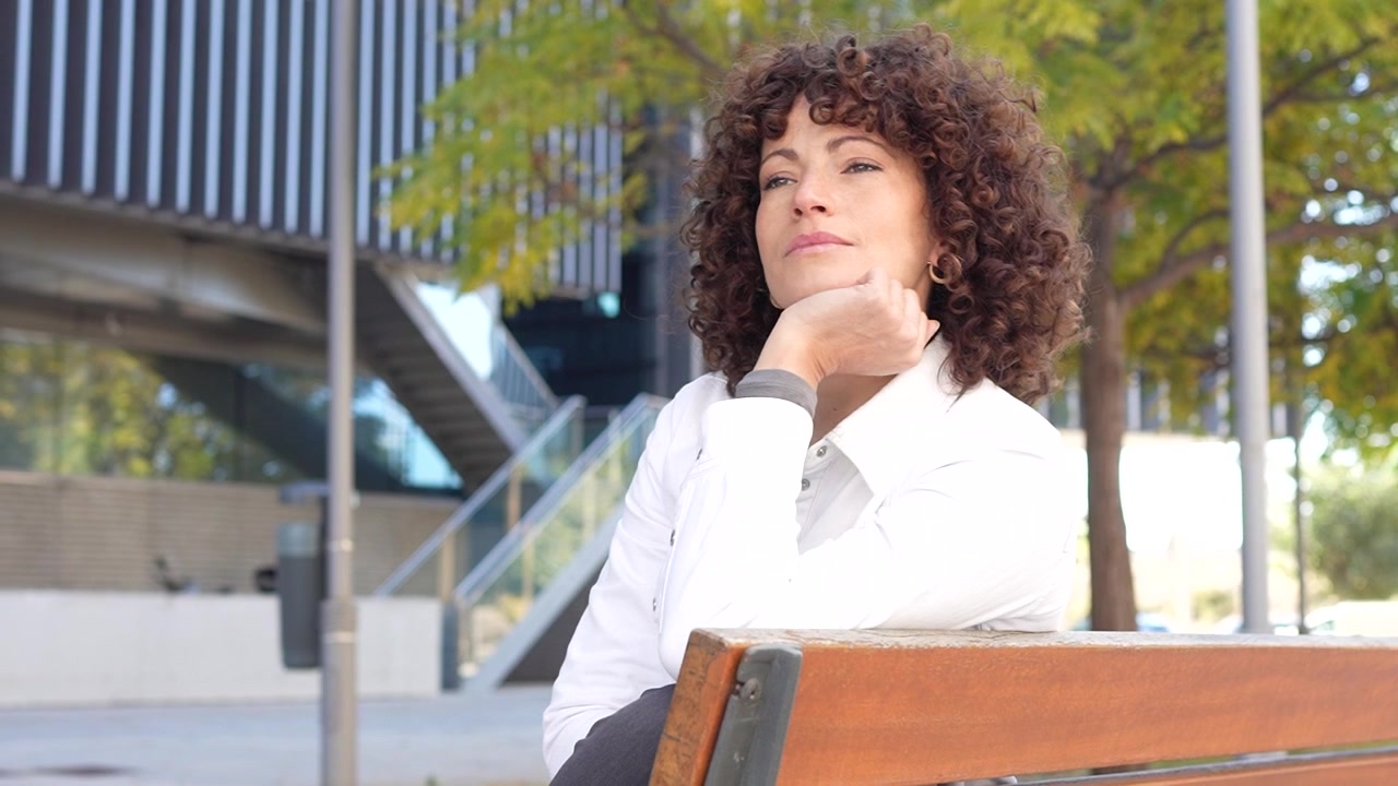 Una donna pensierosa con bellissimi capelli ricci posa elegantemente in un vivace ambiente urbano
