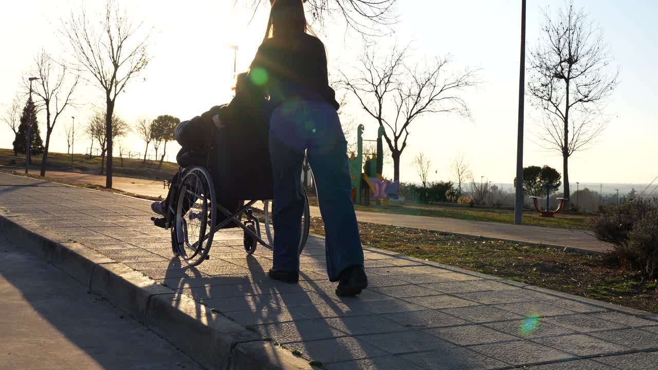 Rear view of girl pushing granny in wheelchair through park at sunset, warm and calm vibe