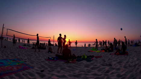 silhouettes of people on a beach playing volleyball at sunset