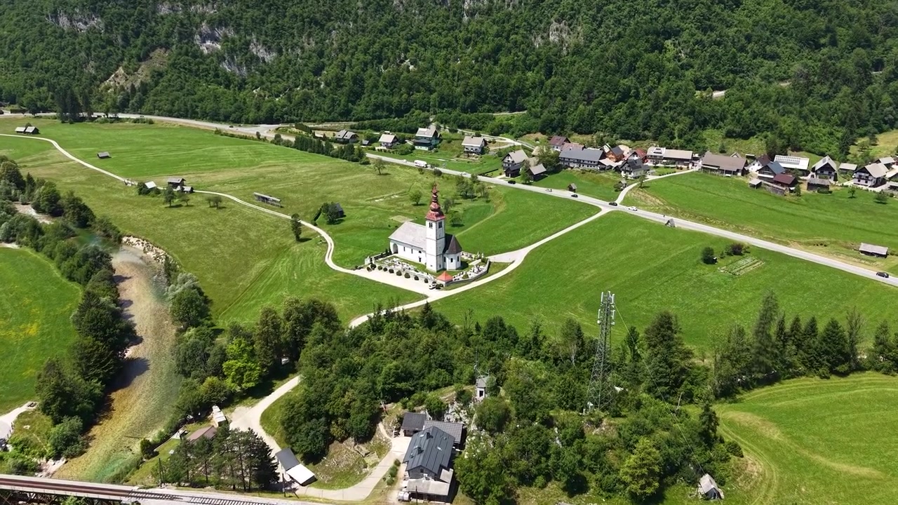 Tomada de drone de igreja de aldeia, edifícios e paisagem verde nas Montanhas dos Alpes, Eslovênia.
