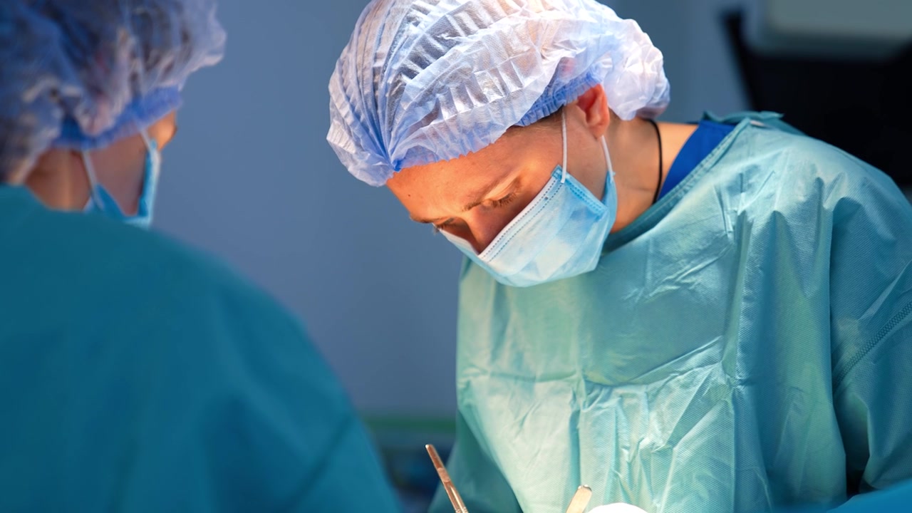 Chirurgo donna caucasica concentrata usa strumenti metallici durante l'operazione. Un'infermiera strumentista non identificata si trova in primo piano