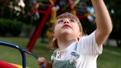 little baby toddler shaking head and hair while spinning at playground carousel