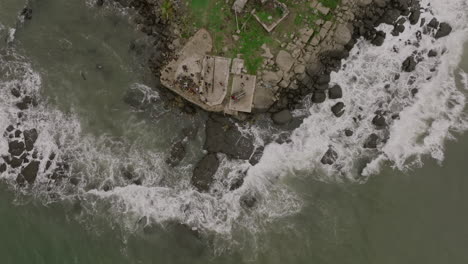 slow motion aerial footage top down of ocean waves crashing into rocks with group of people at the point of a peninsula