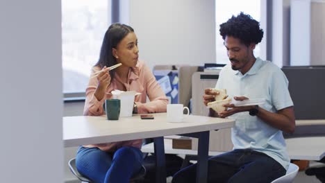 video de una feliz mujer de negocios diversa y un hombre de negocios comiendo y hablando en la oficina