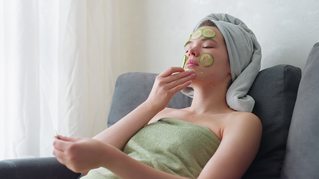 Woman relaxing in towel, placing cucumber slices all over face, enjoying rejuvenating facial treatment, skincare and self-care routine for healthy glowing skin and relaxation