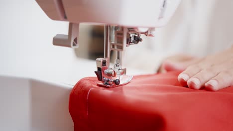 Female-is-using-sewing-machine-with-red-fabric-for-sewing-a-line-on-peace-of-clothing,-textile-industry-manufacturing-concept