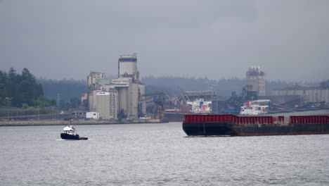 tugboat pulling cargo vessel in harbour on an overcast day