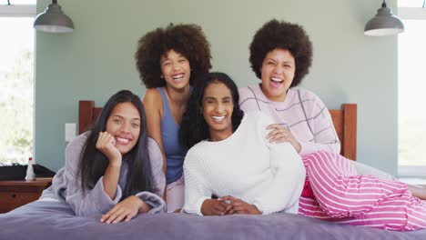 portrait of happy diverse female friends lying on bed and smiling in bedroom