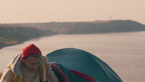 guy-gets-out-of-tent-on-river-bank-stretching-in-morning