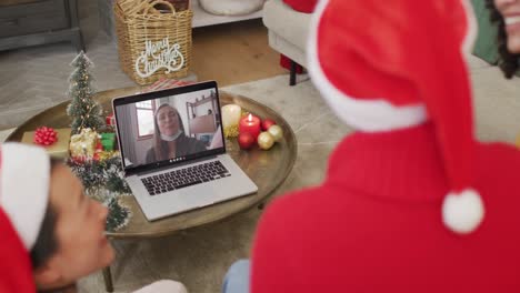 Diverse-family-with-santa-hats-using-laptop-for-christmas-video-call-with-happy-woman-on-screen