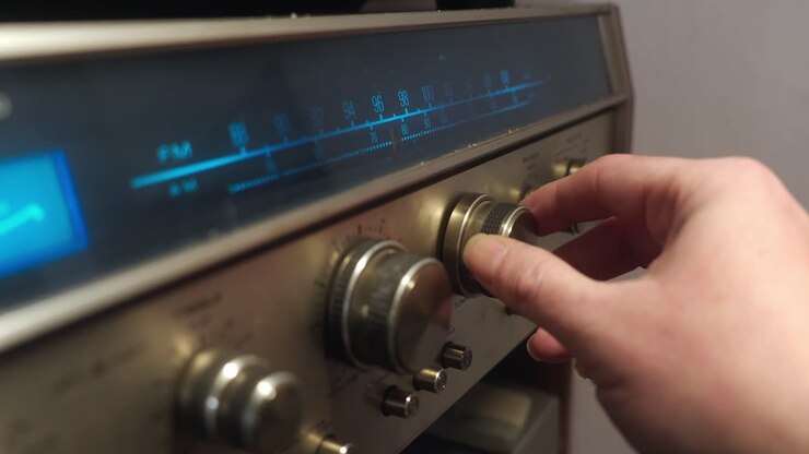 Close-up of a hand turning a knob to change frequency on a retro radio with metal design and blue backlit display