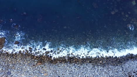 gentle waves breaking along a rocky shoreline - straight down aerial view