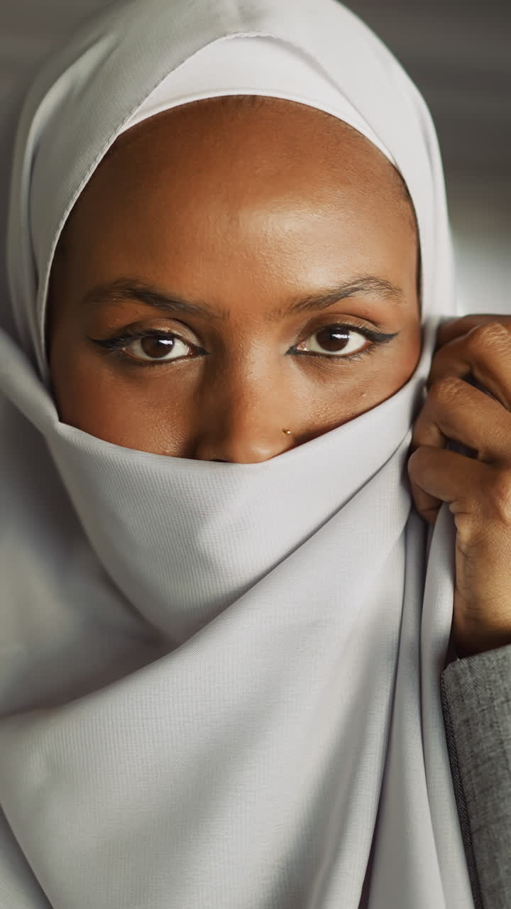 Cheerful African-American woman covers face with hijab on waterfront closeup slow motion. Advanced Muslimah shows traditional accessory in city