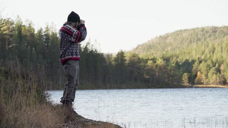 man standing by the lake looking through the binoculars