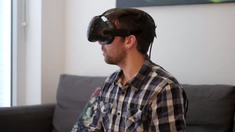 A-medium-shot-of-a-young-white-male-looking-around-with-virtual-reality-while-sitting-on-a-couch