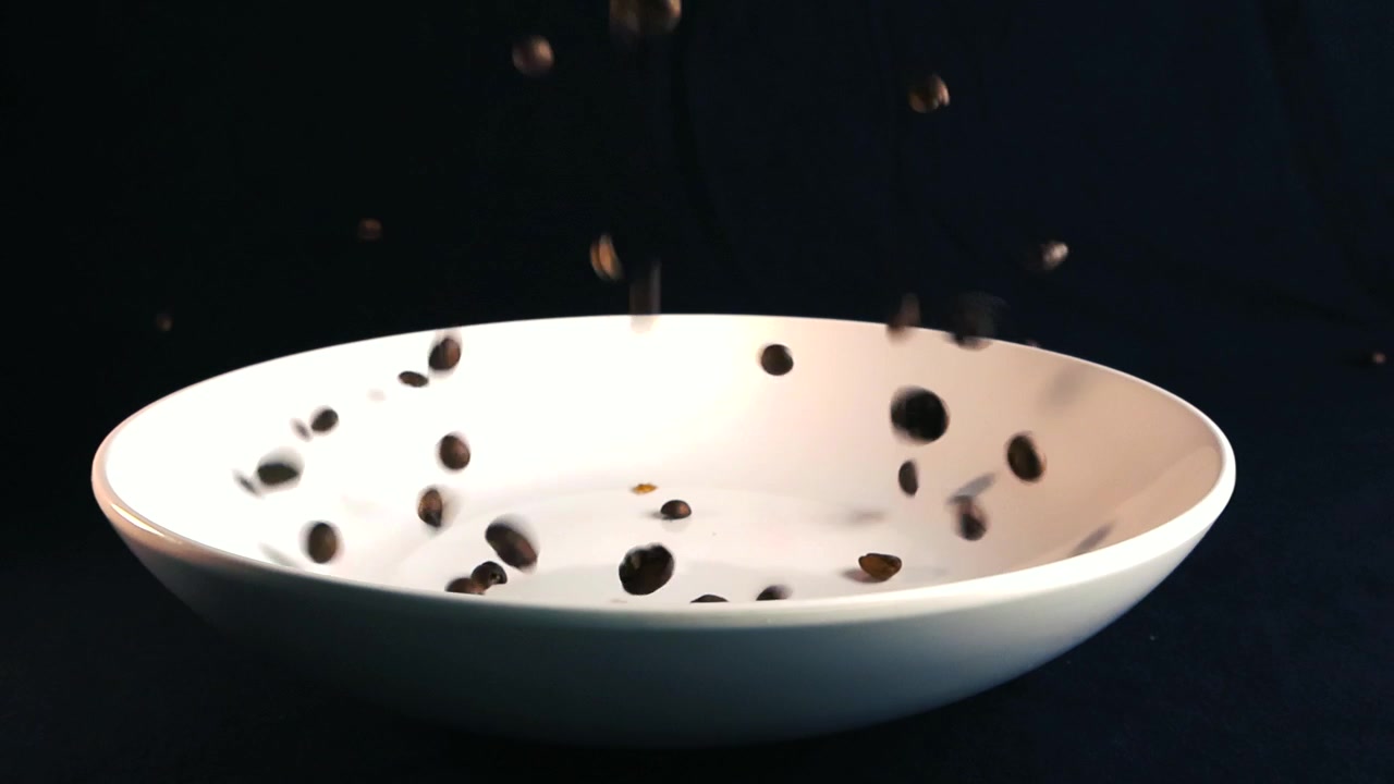 Grãos de café torrados aromáticos a cair e a saltar graciosamente para um prato de cerâmica branco imaculado, capturados em elegante câmara lenta contra um impressionante fundo preto sólido.