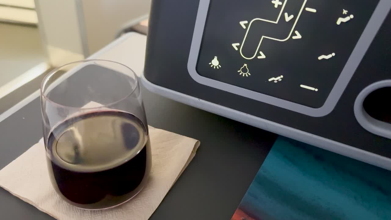 Red wine in glass vibrates on airplane tray table as turbulence occurs, cabin lighting, close-up