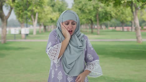 sick muslim woman suffering from tooth pain in park