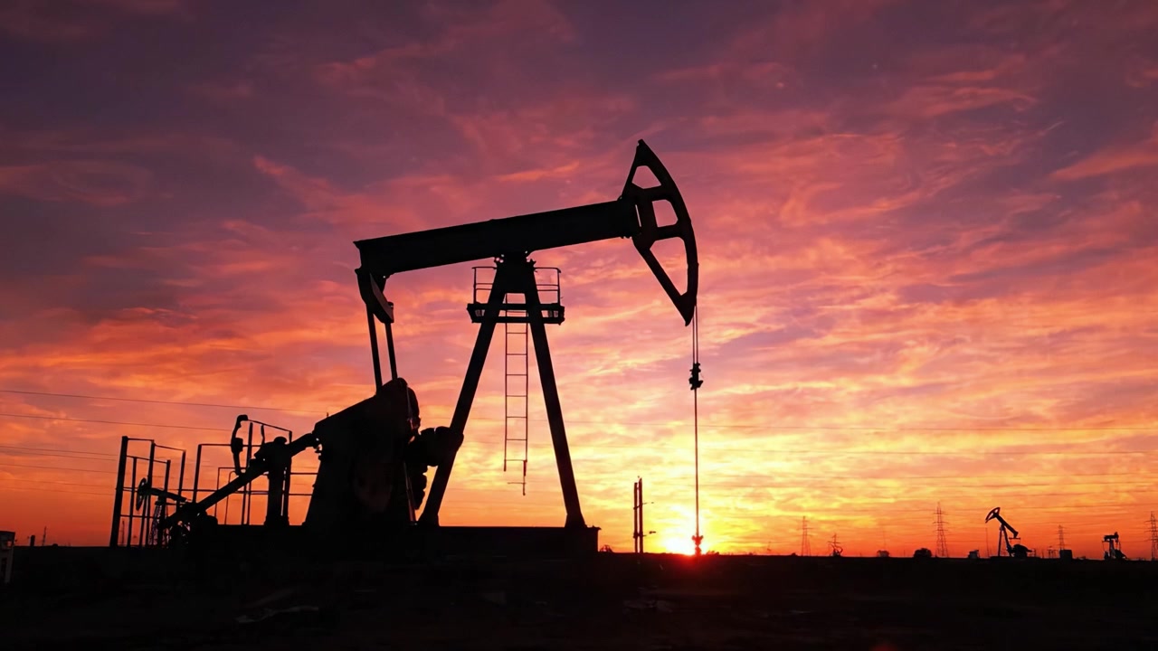 Silhouetted Oil Pump Jacks Against a Breathtaking Sunset Sky with Vibrant Colors, Symbolizing the Intersection of Natural Beauty and Industrial Activity in Energy Production.