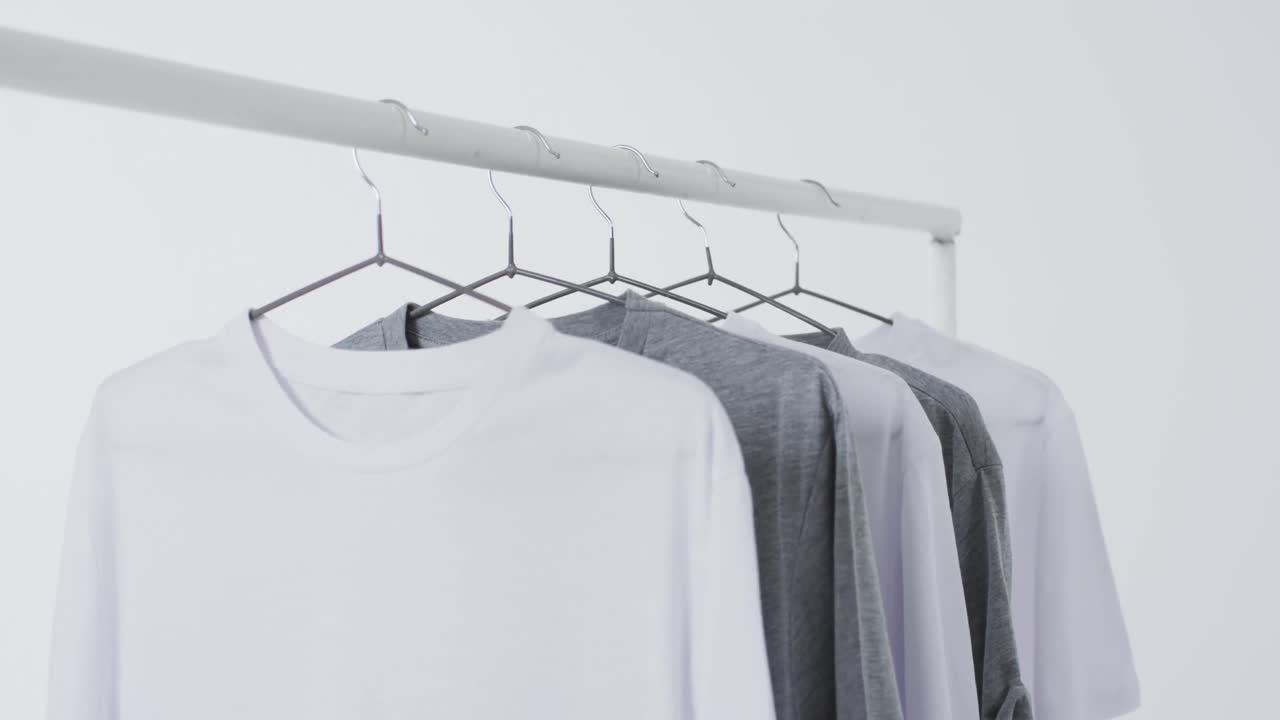 Video of white and grey t shirts on hangers and copy space on white background