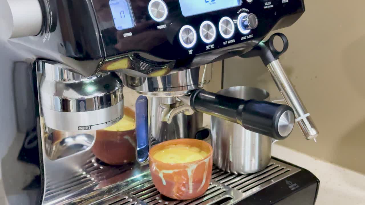 A person operates an espresso machine, brewing coffee in a cozy kitchen setting with soft lighting