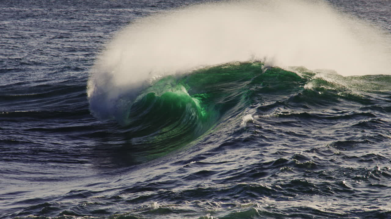 Dramatic ocean wave texture with ocean spray mist rising off top of glowing green wave at sunset
