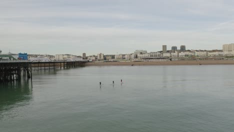 three people on paddle boards heading for the beach in brightonm, seagulls flying past and drone panning right