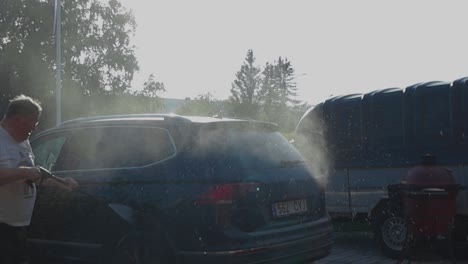 slowly moving footage of a car that gets cleaned with a pressure washer on a house driveway in 4k. sunlight interacting with washing water giving beautiful reflections on a summer day with bright sky.