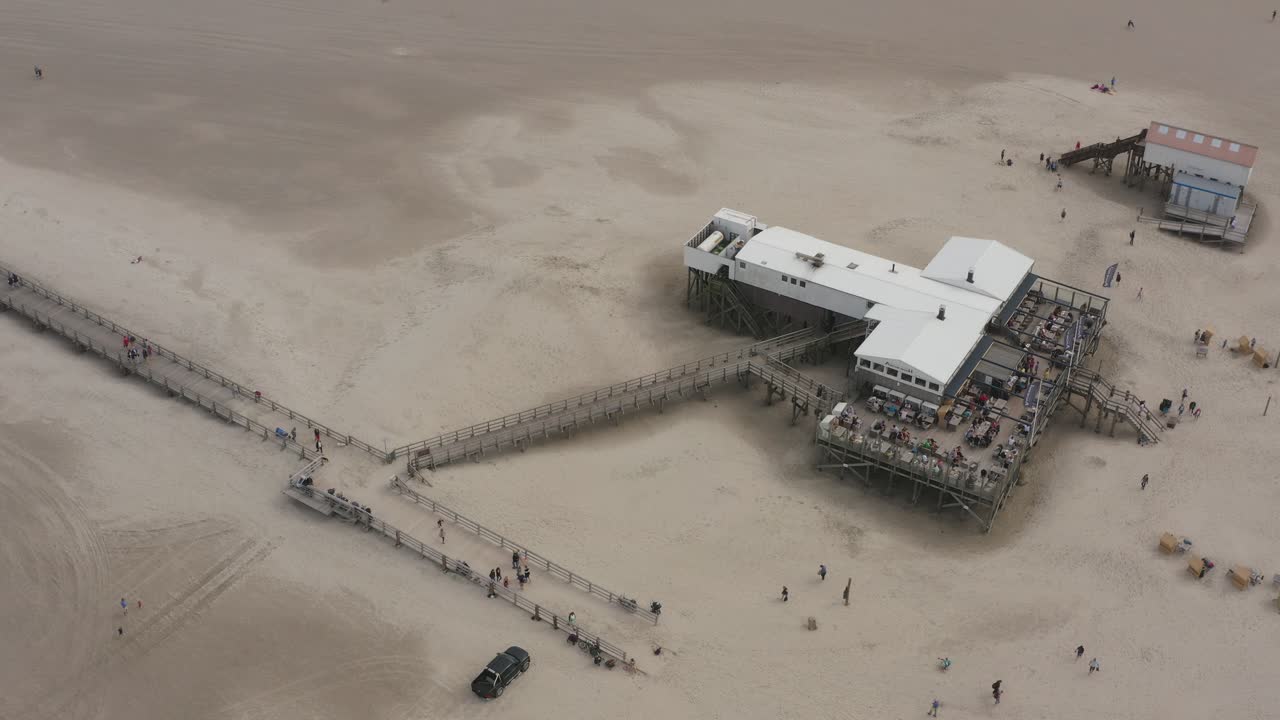 Drone - Aerial top shot of a restaurant, building with the sandy beach with tourists and people in St. Peter Ording at the north sea, schleswig holstein, germany, 25p