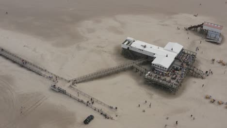 drone - aerial top shot of a restaurant, building with the sandy beach with tourists and people in st. peter ording at the north sea, schleswig holstein, germany, 25p