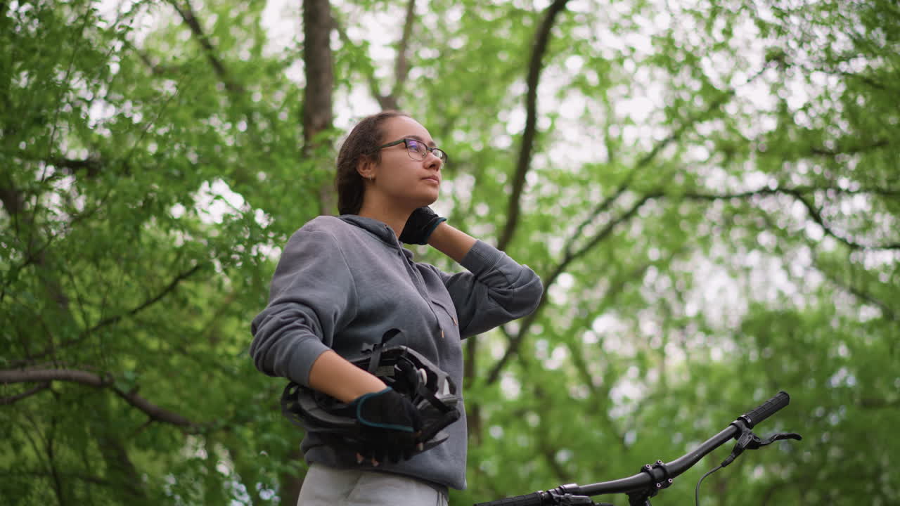 Focused Asian Student Gets Set To Ride, Youthful Rider From Asia Calmly Prepares For Cycling Adventure, Young Asian Athlete Gets Ready To Cycle Beneath Lush Green Foliage With Confidence