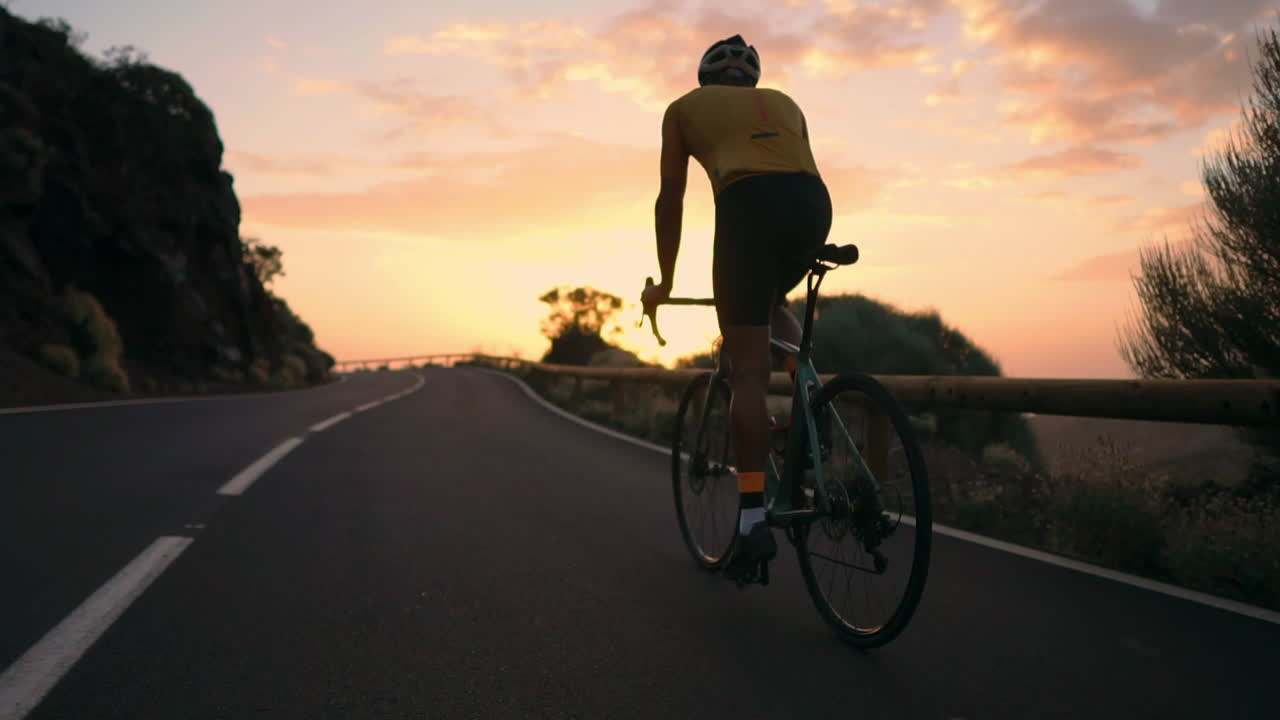 In slow motion, the athlete rides a bike along a mountain serpentine, taking in the island's view, epitomizing a devotion to a healthy lifestyle during sunset
