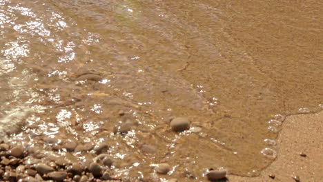 close up of waves rolling up sandy beach with pebbles