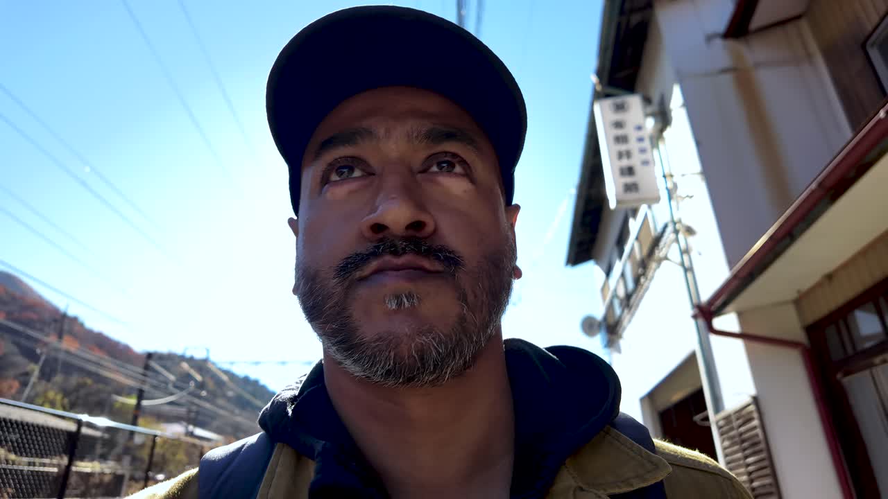 Low angle view of south asian bearded man wearing baseball cap exploring Japan countryside