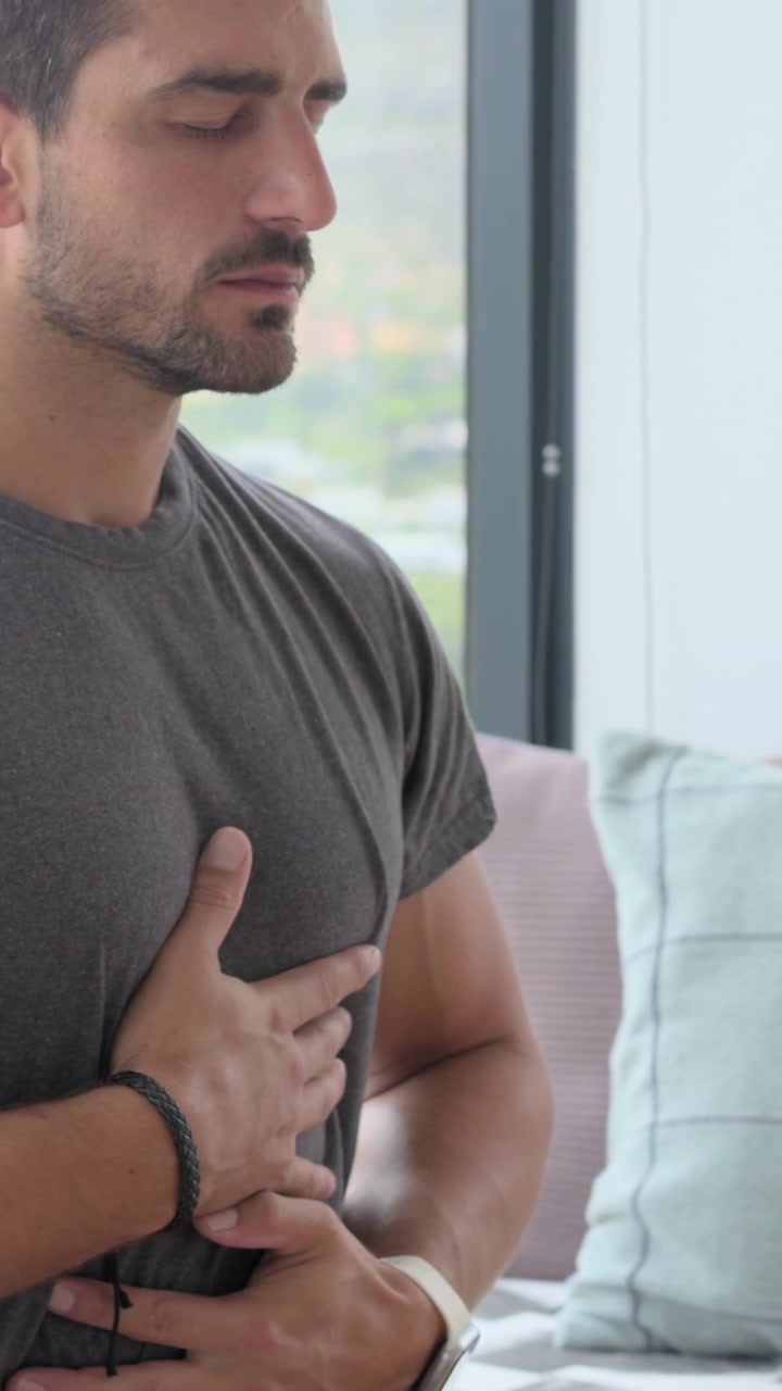 Dikey video: Adam ellerini göğsüne ve karnına koyarak pencere kenarında zindelik için yavaş nefes alıp veriyor.