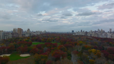 Fly-above-autumn-park.-Colourful-foliage-in-Central-park-surrounded-by-buildings-in-city.-Manhattan,-New-York-City,-USA