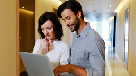 Male-and-Female-executives-using-laptop-in-corridor