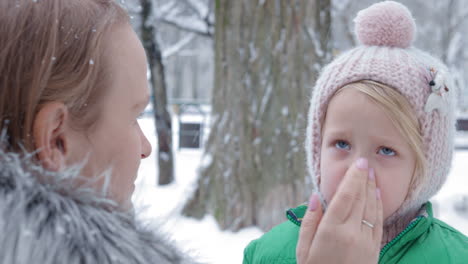 mutter, die an einem wintertag feuchtigkeitscreme auf das gesicht ihrer tochter aufträgt