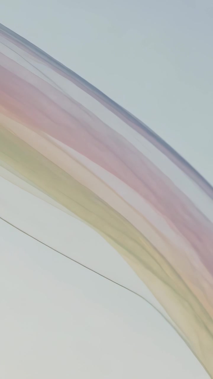 Vertical video: Entering frame from left, sheer ribbon moving across pale sky showing pastel layers