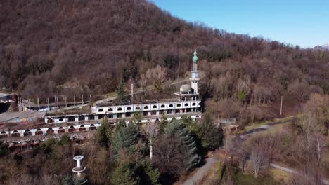 Aerial-view-over-Consonno-a-'ghost-town'-of-Olginate,-Lecco,-in-Lombardy,-vegetation-and-snow-capped-mountains-in-the-background