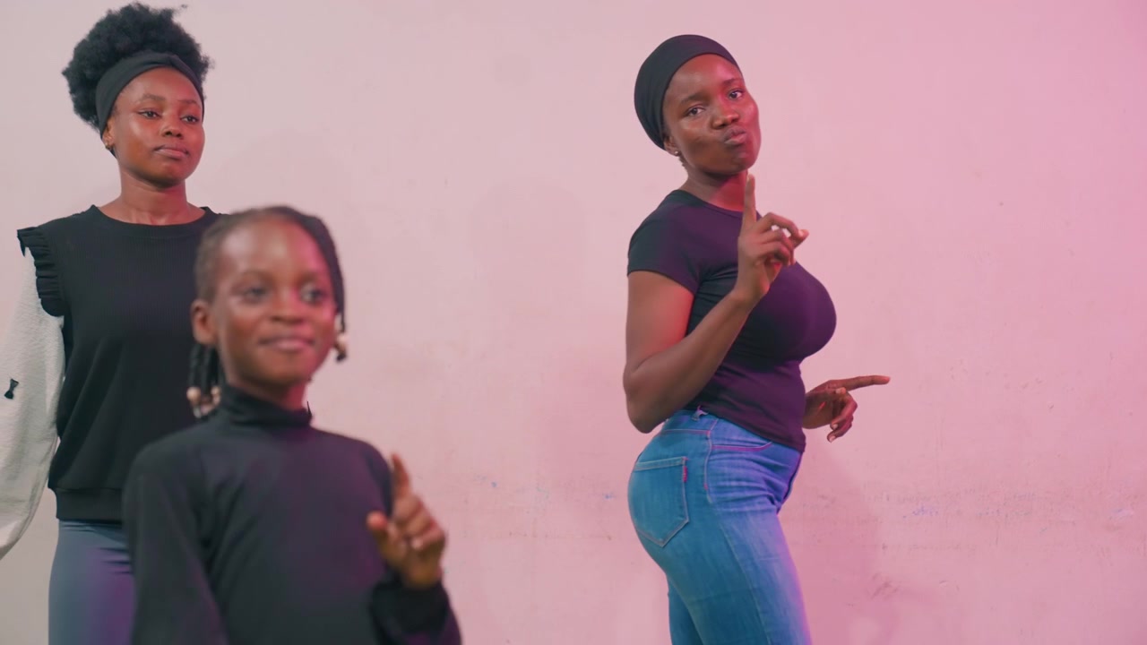 Black mother and child dancing together in pinklit space confident mother as coach and sister as choreographer while young daughter shines in front, upbeat celebration vibe with rhythmic moves, denim