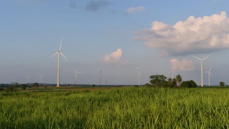 Turbinas-Eólicas-Salen-Disparadas-De-Una-Tierra-De-Cultivo-Mientras-El-Sol-Se-Pone-Mientras-Los-Camiones-Pasan-Haciendo-Nubes-De-Polvo,-Energía-Alternativa-Limpia-En-Tailandia-Y-El-Sudeste-Asiático-Continental