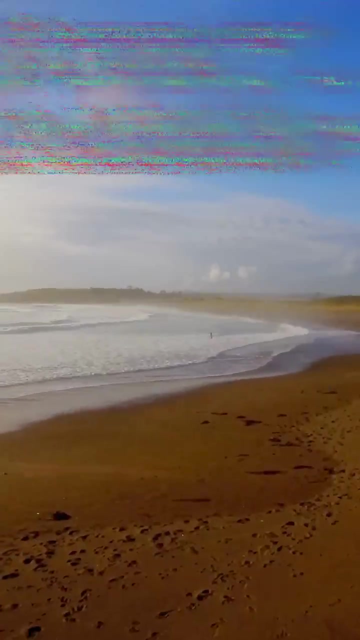 Vertical video: Glitching code causing panning, sandy shore and surf revealing cape to reveal coast