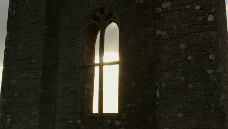 aerial dolly: medieval irish abbey tower backlit by sun, window glows