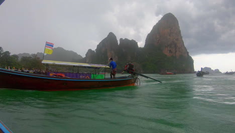 slow motion | a boat in thailand leaving the beach and trying to beat the approaching storm. islands and other boats in the background